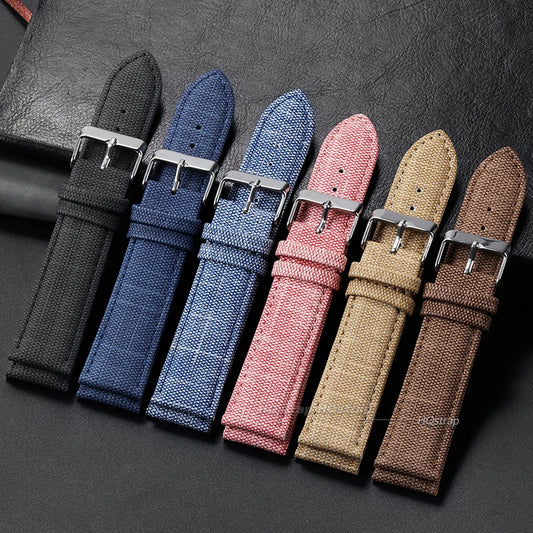 Set of five fabric watch straps in black, blue, pink, beige, and brown on a dark surface.