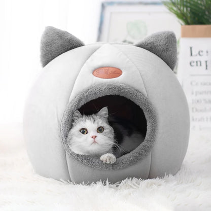 Cat peeking out from a gray and white pet bed with cat ears on a white surface.