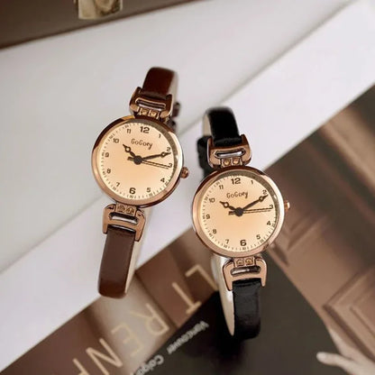 Two watches with gold faces and brown and black straps on a textured surface.