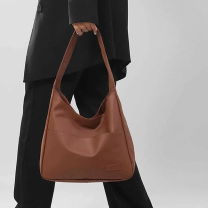Person holding a brown leather handbag against a plain background