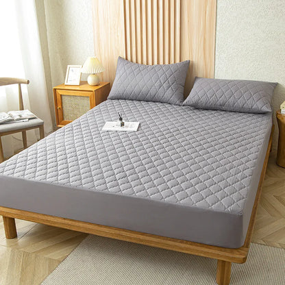 Gray quilted mattress cover on a wooden bed in a bedroom setting.