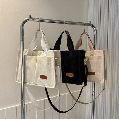 Three bags hanging on a rack against a neutral wall.
