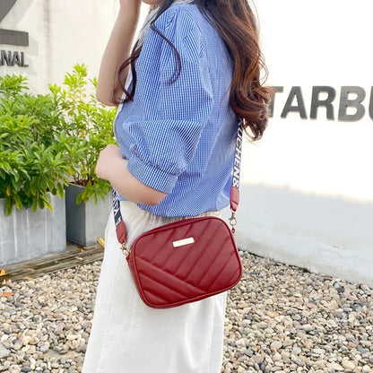 Person wearing a blue shirt and white pants with a red quilted handbag, standing outdoors.