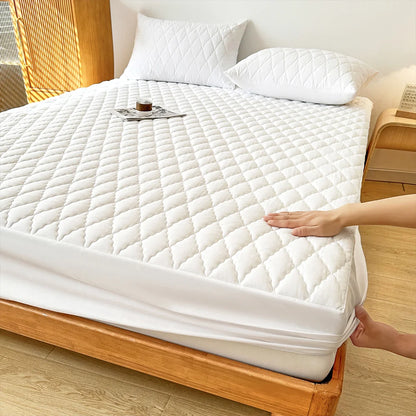 Person adjusting a white mattress protector on a wooden bed in a bedroom.
