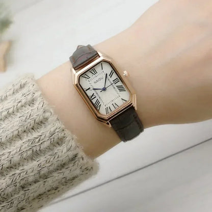 Wrist wearing a watch with a brown strap and rose gold case on a light background