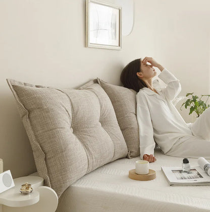 Woman sitting on a bed with large pillows, looking relaxed.