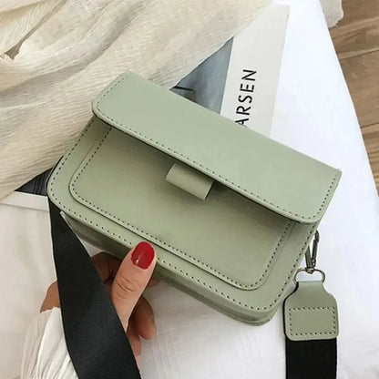 Green handbag held by a hand with red nail polish on a light background
