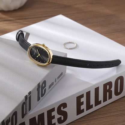 Black watch with gold case on a book titled 'MES ELLRO' on a wooden surface