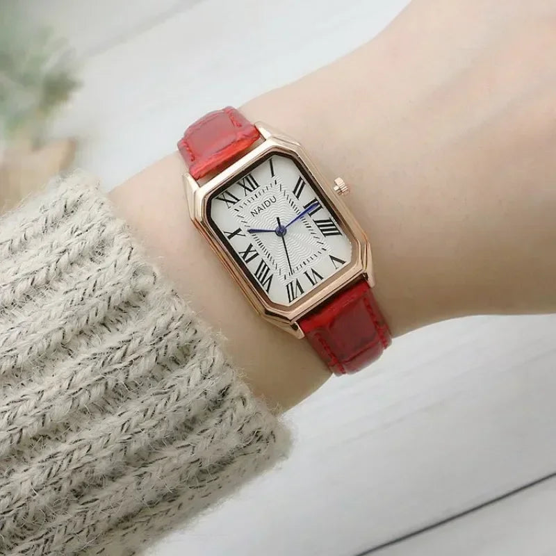 Wristwatch with red strap and white face on a wrist, wearing a textured sleeve.