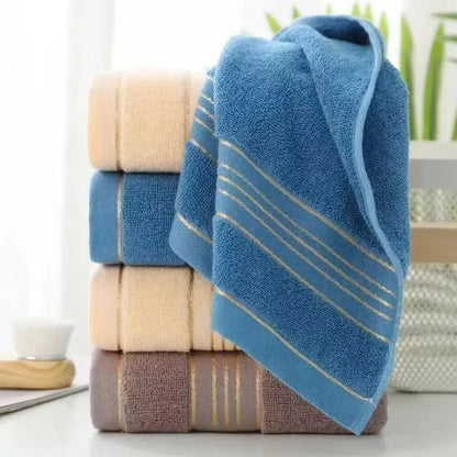 Stack of blue, beige, and brown striped towels on a white surface with a blurred plant in the background.