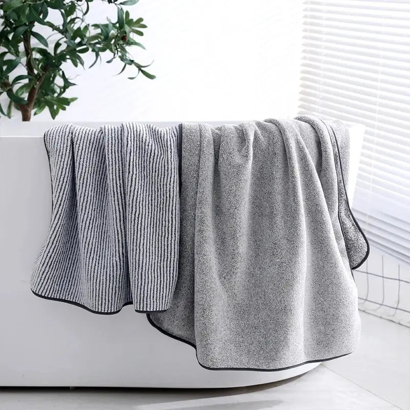 Gray towel draped over a white bathtub with a plant in the background