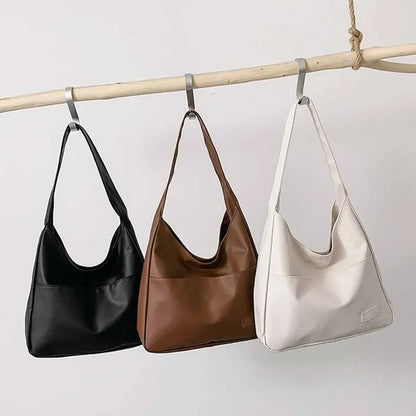 Three handbags in black, brown, and beige hanging on a rod against a light background.
