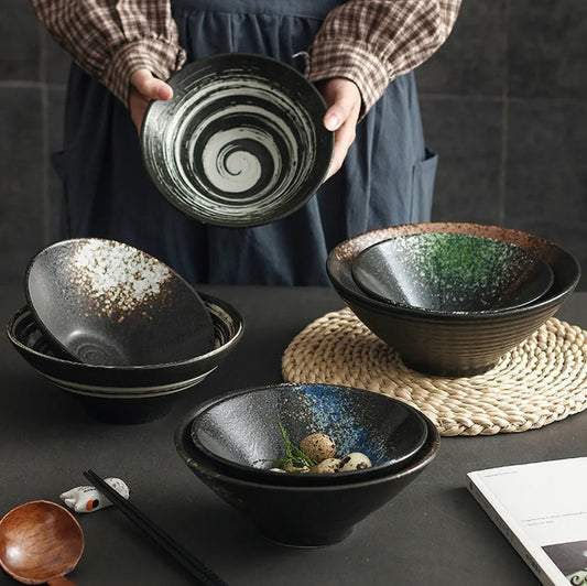 Person holding a black ceramic bowl with a swirling design on a dark surface with other bowls.