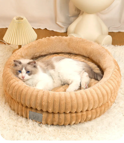 Cat lying in a beige pet bed with a lamp and decorative item in the background