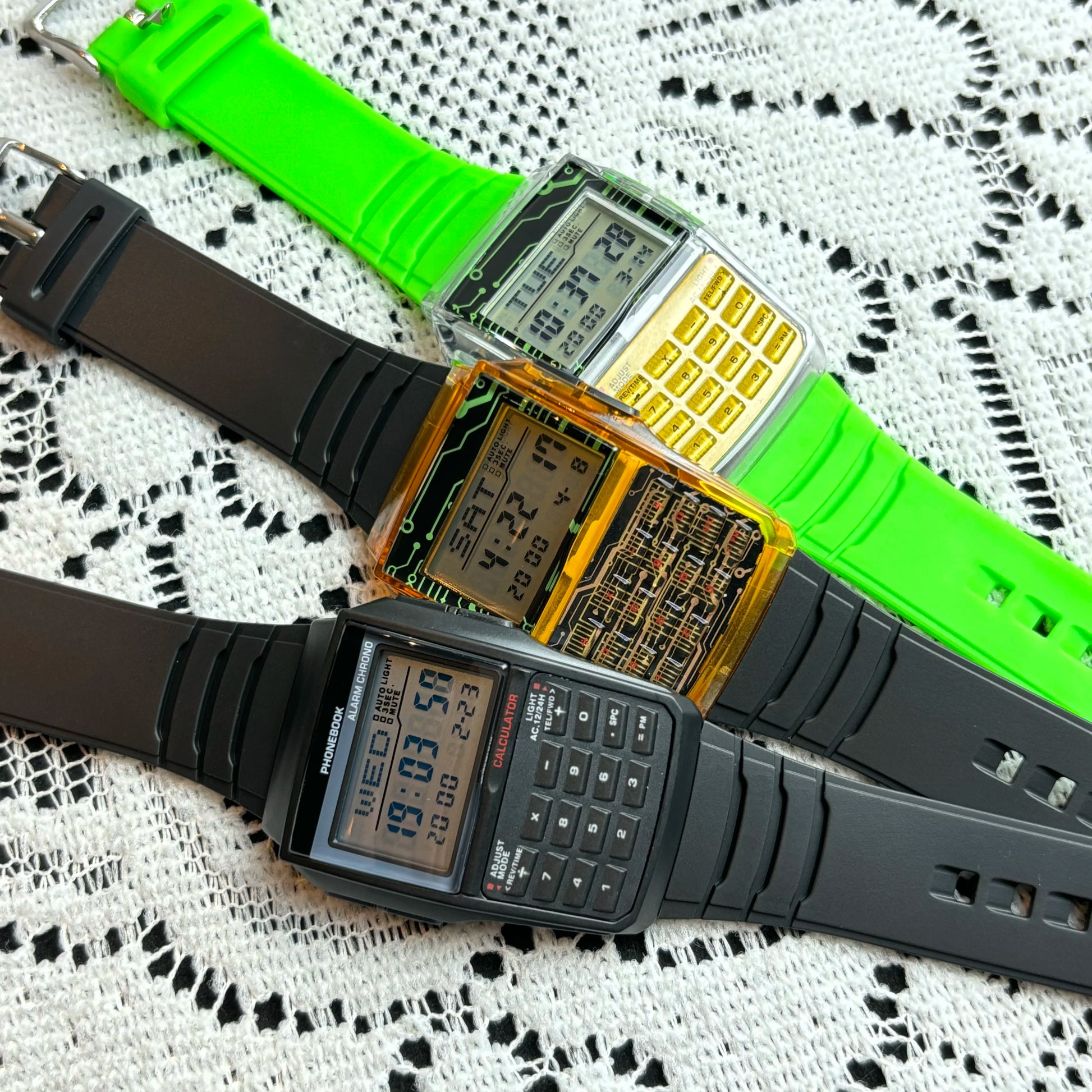 Two digital wristwatches with green and black straps on a lace background