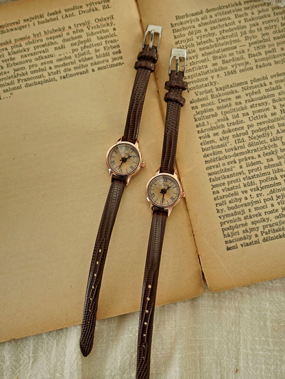 Two vintage-style wristwatches with brown straps on an old book page.