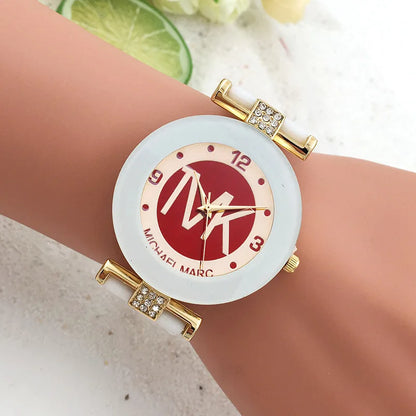 Gold watch with a red face on a wrist, brand 'MK' visible
