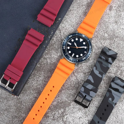 Watch with orange strap and black dial, surrounded by additional straps on a textured surface