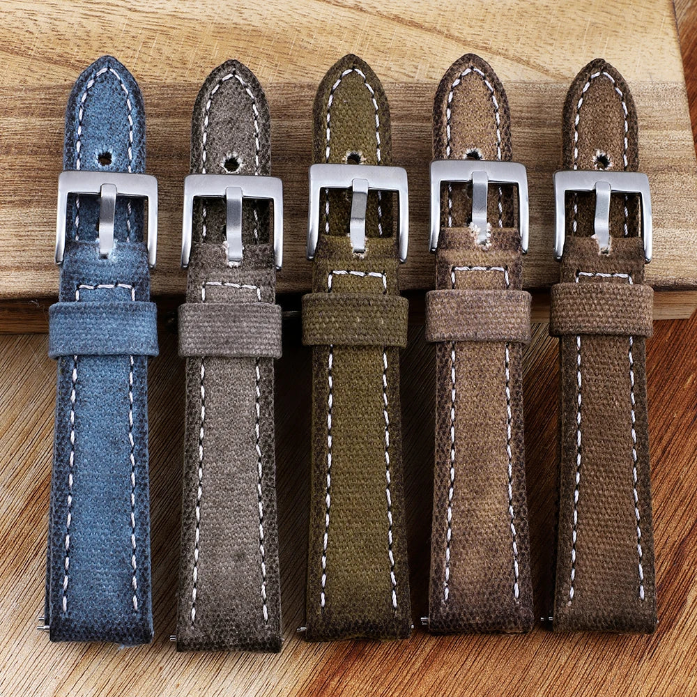 Five watch straps in blue, gray, green, brown, and brown with silver buckles on a wooden surface.