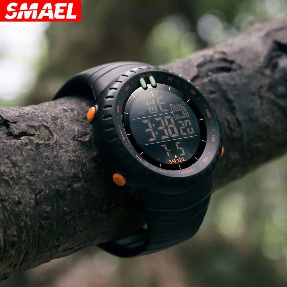 Black digital watch with orange accents on a tree branch, featuring the SMAEL brand.