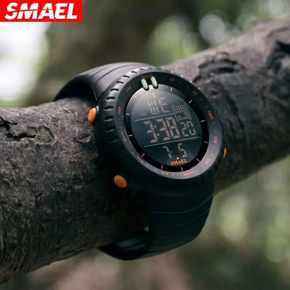 Black digital watch with orange accents on a tree branch, featuring the SMAEL brand.