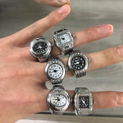 Multiple watches on a person's fingers against a neutral background
