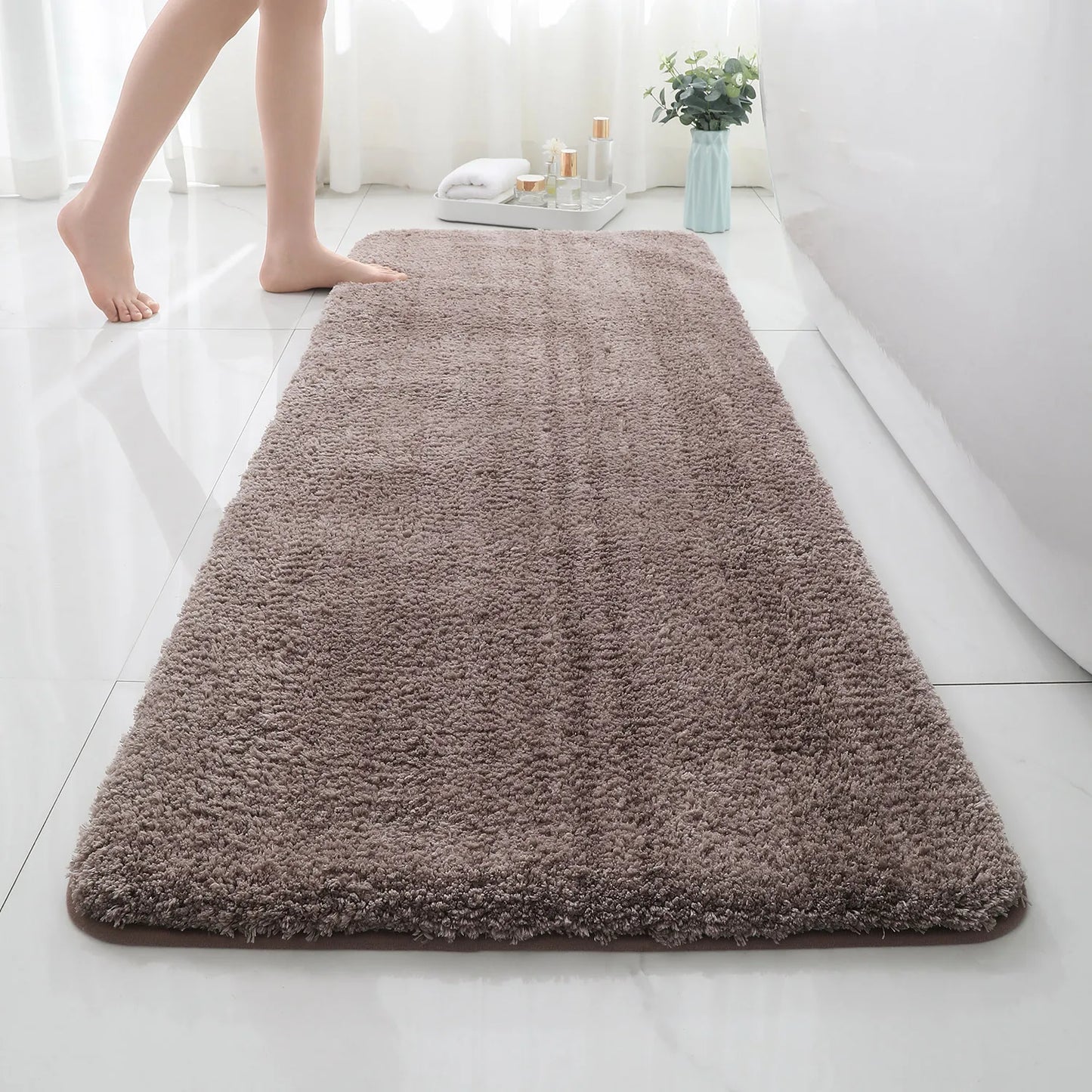 Brown bath mat on a bathroom floor with a person stepping onto it.