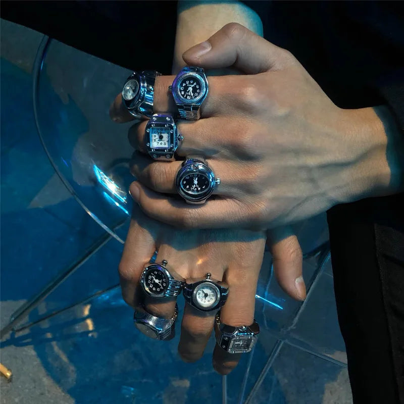 Hand wearing multiple rings with watch faces on a reflective surface