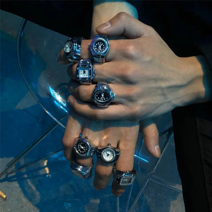 Hand wearing multiple rings with watch faces on a reflective surface