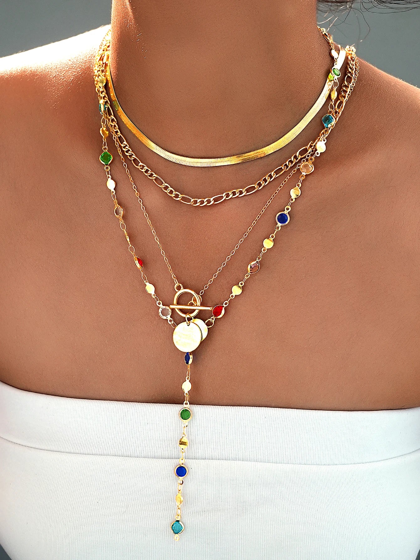 Layered gold necklaces with colorful beads on a person wearing a white top.