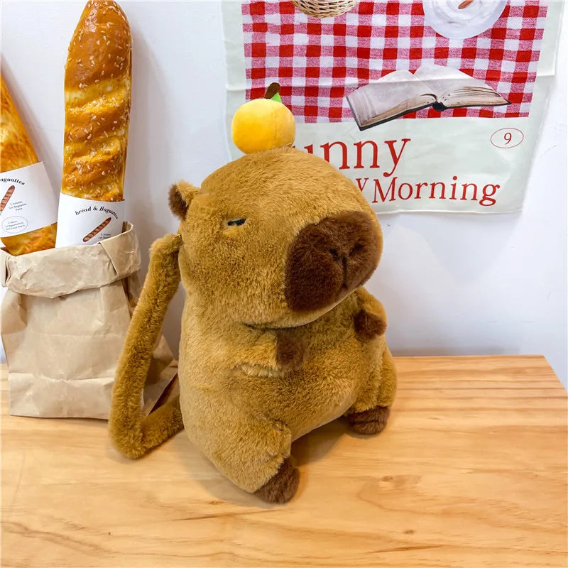 Plush dog toy with a lemon on its head next to a baguette and a book titled 'Happy Morning' on a wooden surface.