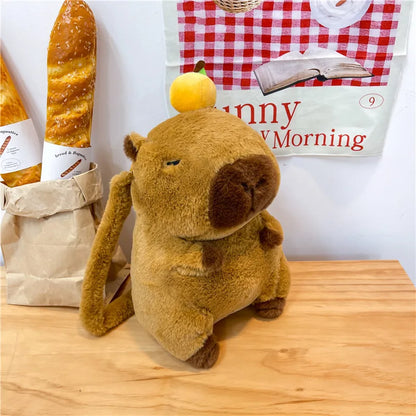 Plush dog toy with a lemon on its head next to a baguette and a book titled 'Happy Morning' on a wooden surface.
