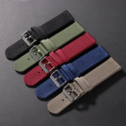 Set of five woven watch straps in black, green, red, blue, and beige on a dark gray background.