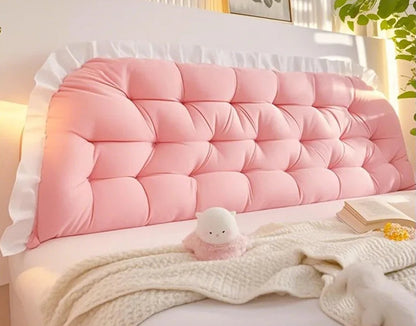 Pink tufted headboard pillow on a bed with a soft blanket and plush toy.