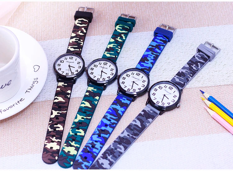Four watches with camouflage straps on a textured surface with a cup and pencils.