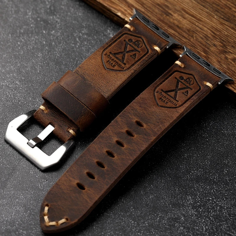 Brown leather watch strap with metal buckle on a dark surface